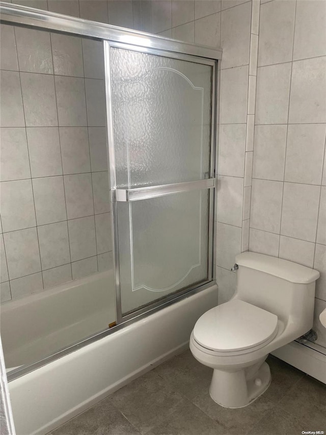 bathroom featuring toilet, enclosed tub / shower combo, tile walls, and tile patterned floors