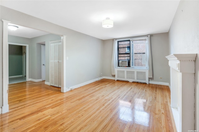 unfurnished living room with cooling unit, radiator heating unit, and light hardwood / wood-style flooring