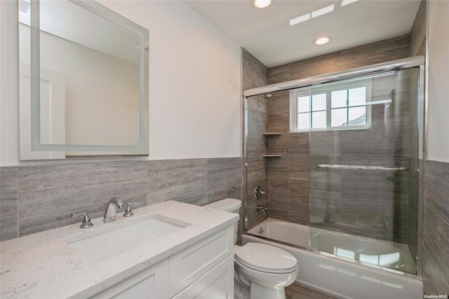 full bathroom featuring shower / bath combination with glass door, vanity, toilet, and tile walls