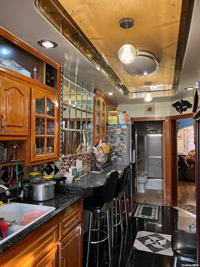 bar with sink, tile patterned floors, dark stone countertops, decorative light fixtures, and a tray ceiling