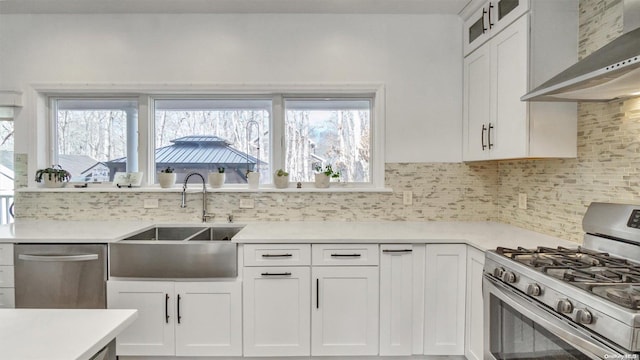 kitchen with decorative backsplash, stainless steel appliances, sink, wall chimney range hood, and white cabinets