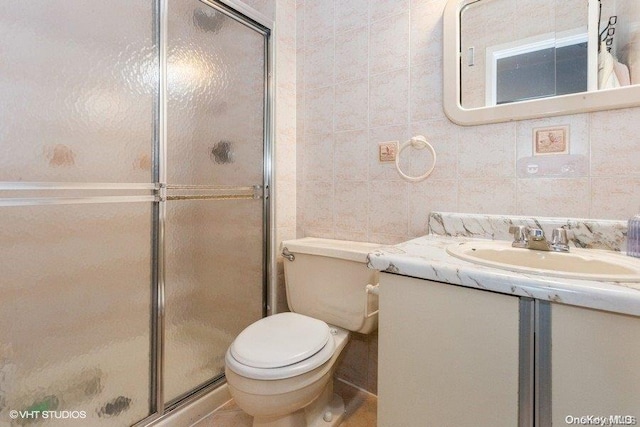 bathroom featuring vanity, a shower with shower door, tile walls, and toilet