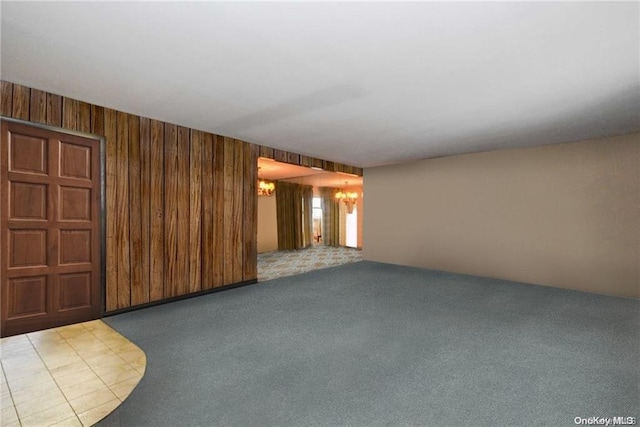 carpeted spare room with a chandelier and wood walls