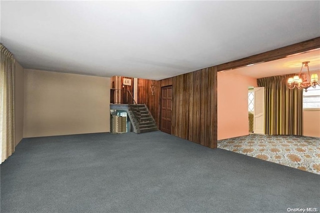 unfurnished living room featuring carpet, wood walls, and a chandelier