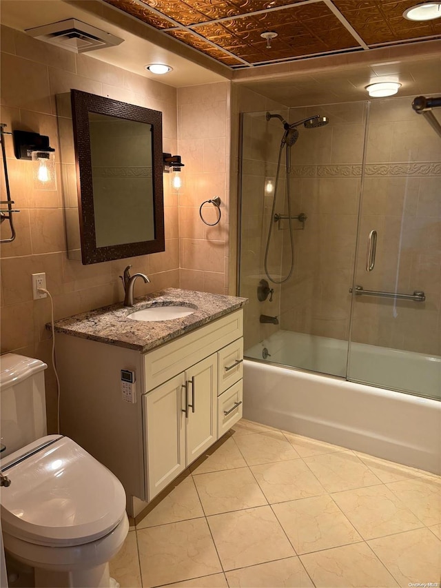 full bathroom with enclosed tub / shower combo, tile patterned floors, toilet, vanity, and tile walls