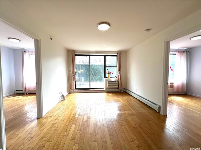 unfurnished room featuring a healthy amount of sunlight, baseboard heating, and light hardwood / wood-style flooring