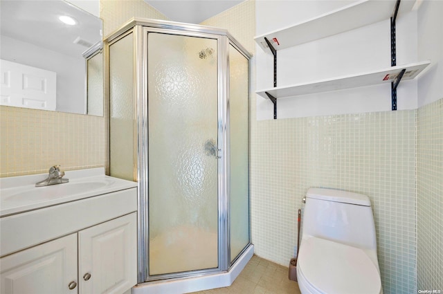 bathroom with vanity, a shower with door, tile patterned floors, toilet, and tile walls