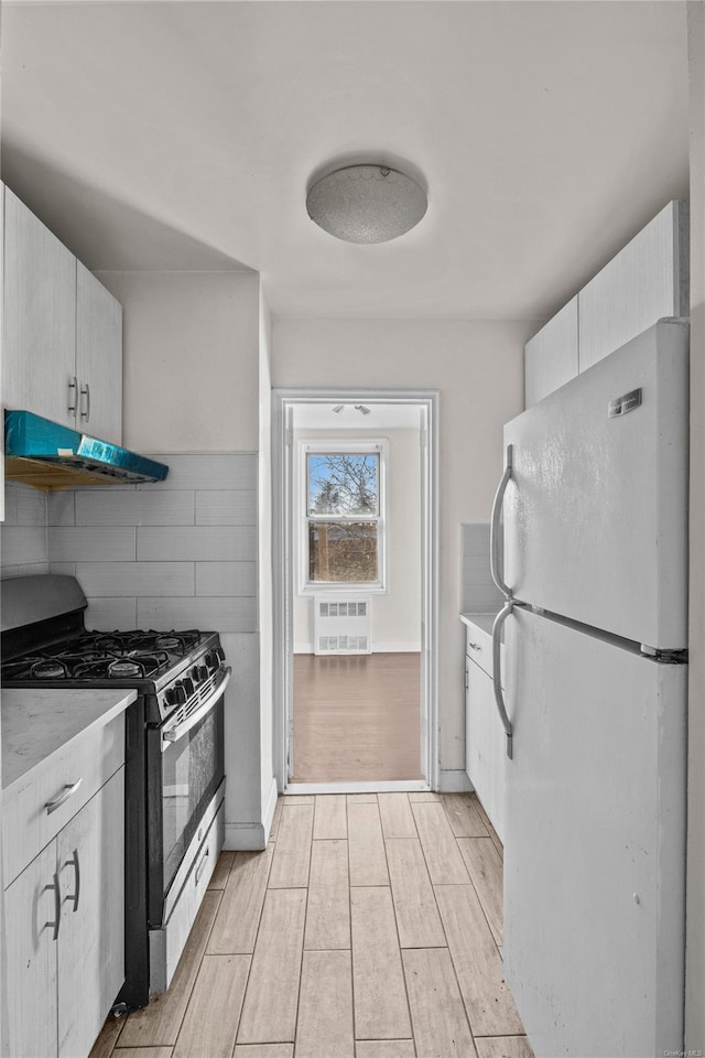 kitchen with white cabinets, white fridge, light hardwood / wood-style floors, and gas range