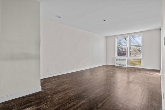 empty room with radiator heating unit, a wall mounted air conditioner, and dark hardwood / wood-style floors