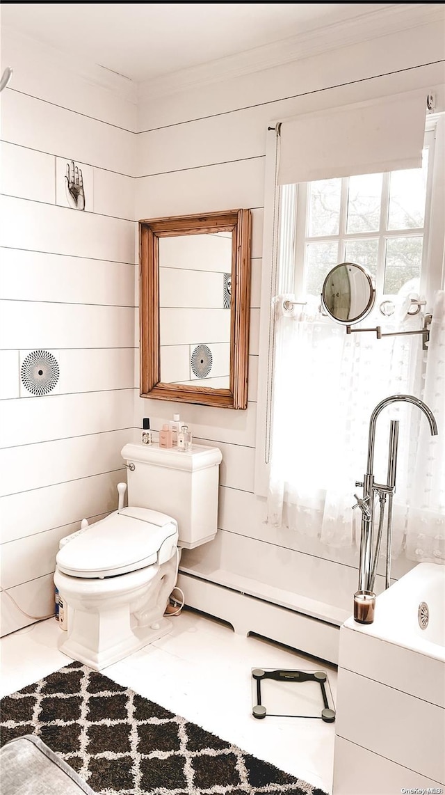 bathroom featuring tile patterned floors, a washtub, baseboard heating, wooden walls, and toilet