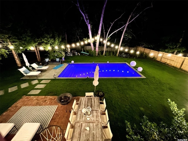 pool at night with a lawn, a patio area, and an outdoor fire pit