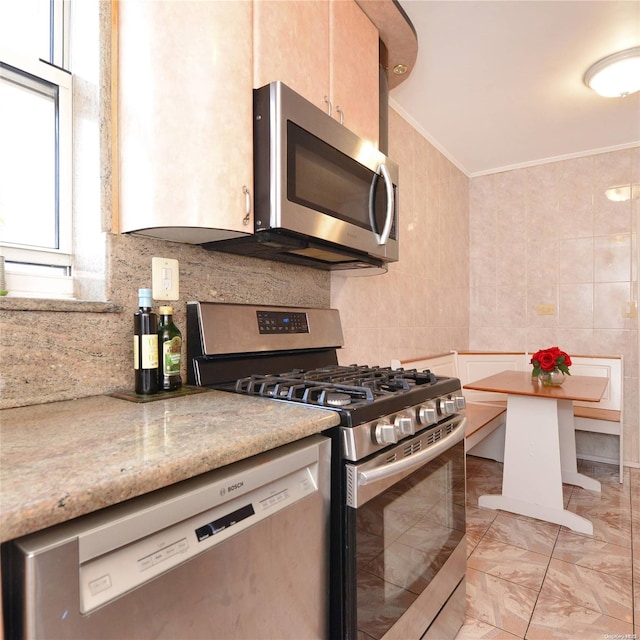 kitchen featuring light stone countertops, stainless steel appliances, tile walls, and ornamental molding