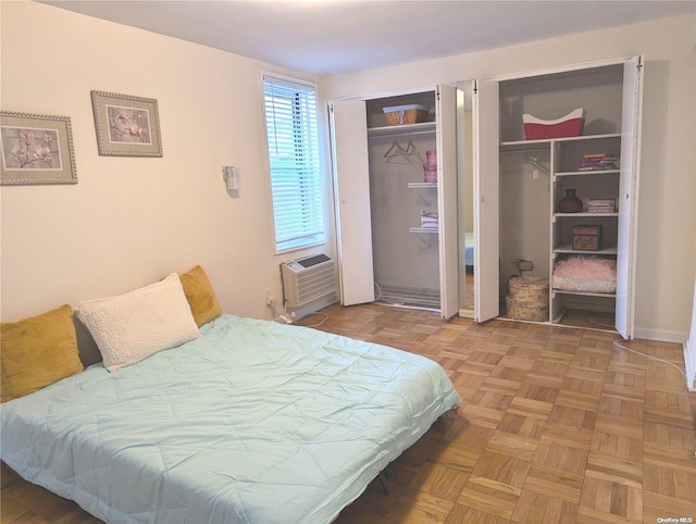 bedroom with parquet flooring, two closets, and a wall mounted AC