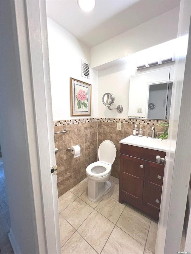 bathroom with tile patterned flooring, vanity, toilet, and tile walls