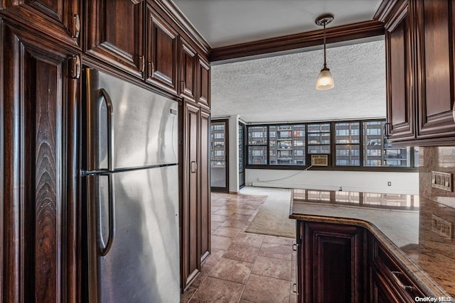 kitchen with pendant lighting, dark stone countertops, a textured ceiling, dark brown cabinetry, and stainless steel refrigerator