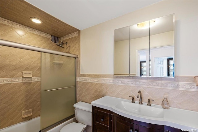 full bathroom featuring vanity, toilet, tile walls, and bath / shower combo with glass door