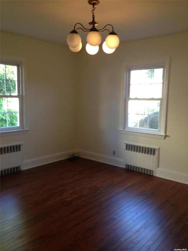 spare room featuring radiator heating unit, dark hardwood / wood-style flooring, and a notable chandelier