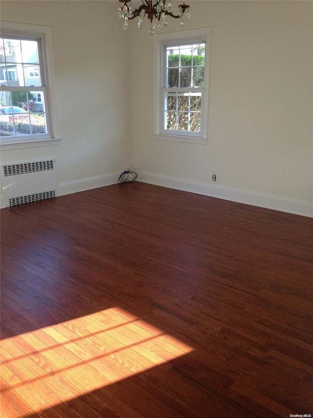 spare room featuring plenty of natural light, radiator, dark wood-type flooring, and a notable chandelier