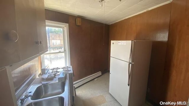 kitchen featuring sink, white fridge, baseboard heating, and wood walls