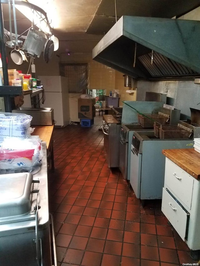 kitchen with butcher block countertops, dark tile patterned floors, white fridge, and exhaust hood