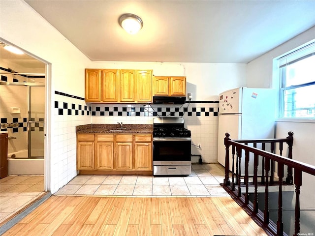 kitchen with sink, range hood, white refrigerator, stainless steel range with gas stovetop, and light wood-type flooring