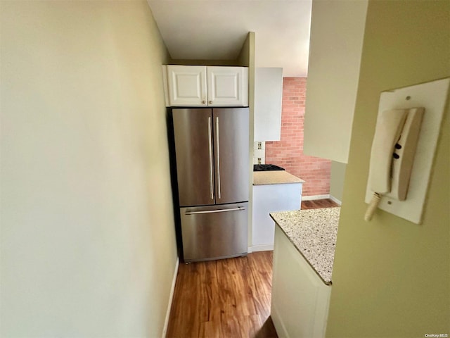 kitchen with light stone counters, gas stovetop, white cabinets, light hardwood / wood-style floors, and stainless steel refrigerator