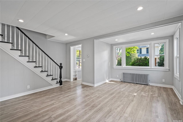 unfurnished living room with wood walls, radiator heating unit, light hardwood / wood-style floors, and plenty of natural light