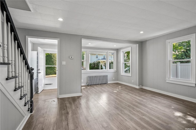 unfurnished living room featuring radiator heating unit, a healthy amount of sunlight, and hardwood / wood-style floors