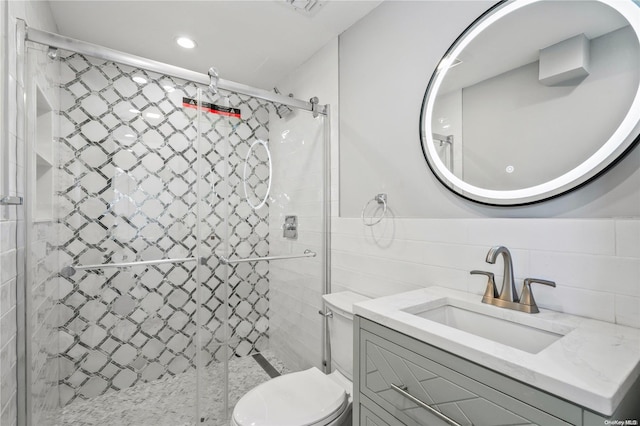 bathroom with vanity, toilet, a shower with door, and tile walls