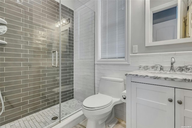 bathroom featuring vanity, toilet, a shower with shower door, and tile walls