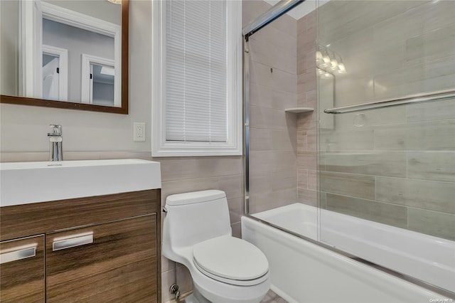 full bathroom featuring vanity, toilet, shower / bath combination with glass door, and tile walls