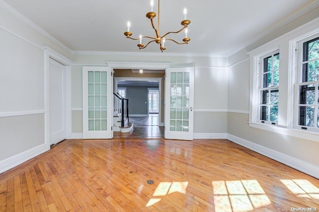 unfurnished dining area with a chandelier, ornamental molding, light hardwood / wood-style flooring, and french doors