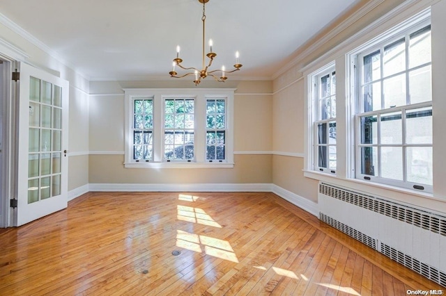 unfurnished dining area featuring radiator heating unit, light hardwood / wood-style flooring, ornamental molding, and a notable chandelier