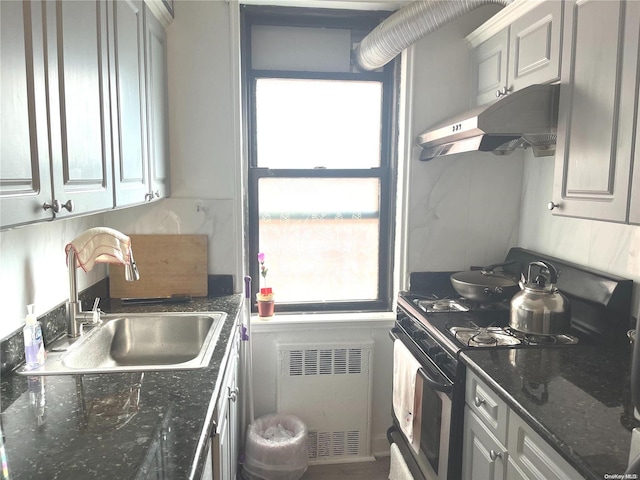 kitchen featuring gas stove, radiator, dark stone countertops, and sink