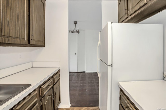 kitchen featuring dark brown cabinetry, sink, white fridge, and a notable chandelier