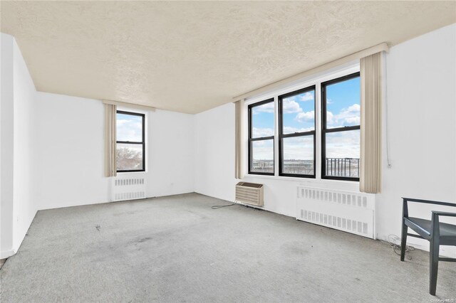 carpeted empty room with a textured ceiling, radiator, and a wall mounted AC