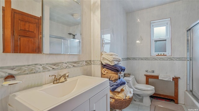 full bathroom featuring combined bath / shower with glass door, vanity, tile walls, tile patterned flooring, and toilet