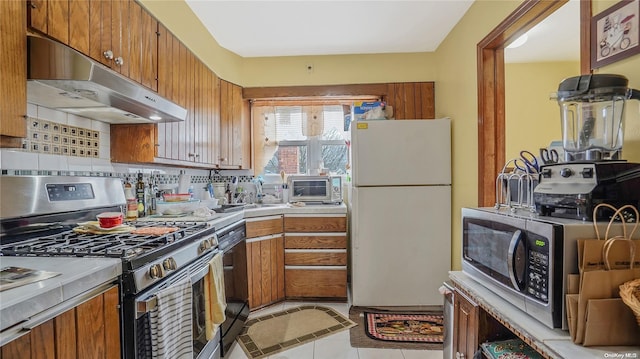 kitchen with backsplash, exhaust hood, white refrigerator, stainless steel range with gas cooktop, and light tile patterned floors