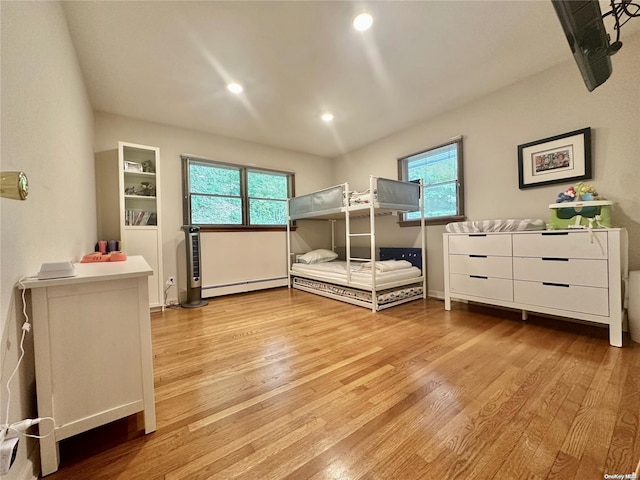 bedroom featuring light hardwood / wood-style flooring, multiple windows, and a baseboard heating unit