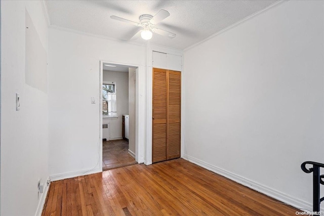 unfurnished bedroom with ceiling fan, ornamental molding, a textured ceiling, wood-type flooring, and a closet