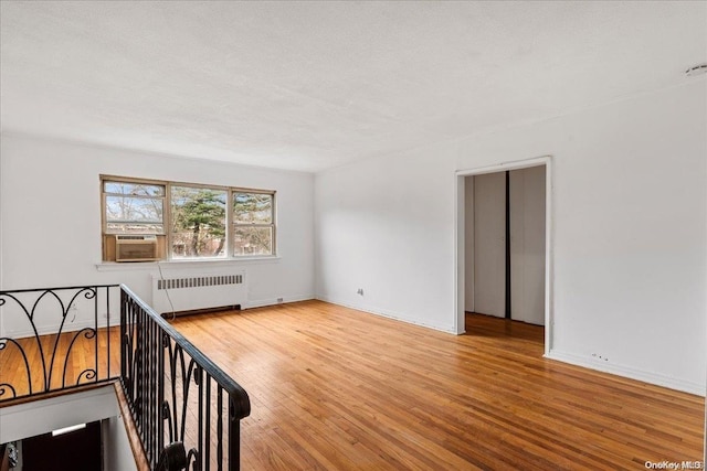 spare room with cooling unit, light wood-type flooring, radiator heating unit, and a textured ceiling