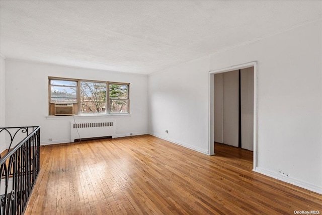 spare room with radiator, cooling unit, a textured ceiling, and light wood-type flooring