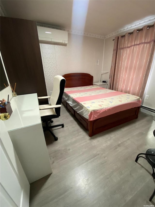 bedroom with a baseboard heating unit, light wood-type flooring, and a wall mounted AC