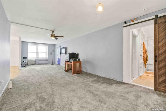 unfurnished living room with a barn door, ceiling fan, radiator heating unit, and light colored carpet