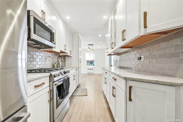 kitchen featuring light stone countertops, tasteful backsplash, stainless steel appliances, light hardwood / wood-style flooring, and white cabinets