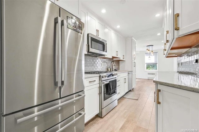 kitchen featuring radiator heating unit, light stone counters, appliances with stainless steel finishes, white cabinets, and light wood-type flooring