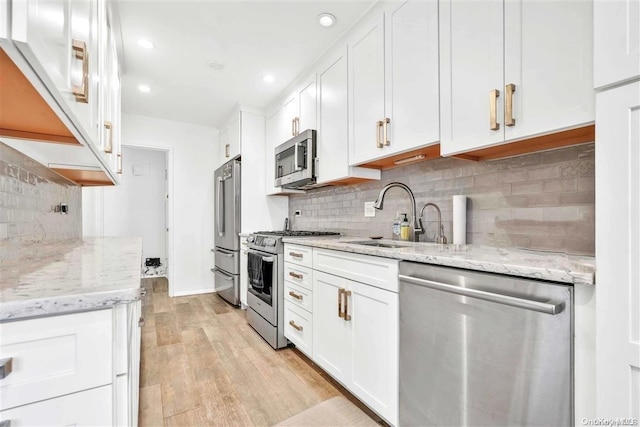 kitchen with appliances with stainless steel finishes, light wood-type flooring, light stone counters, sink, and white cabinets