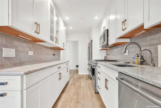 kitchen with white cabinetry, light stone counters, decorative backsplash, appliances with stainless steel finishes, and light wood-type flooring