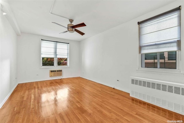 unfurnished room with a wall mounted AC, ceiling fan, radiator heating unit, and light hardwood / wood-style flooring