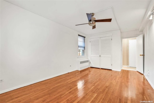 unfurnished bedroom with a closet, ceiling fan, radiator heating unit, and light wood-type flooring